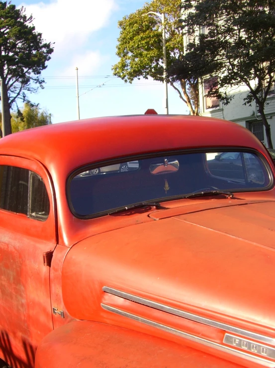 an old, rusted red car is parked near some buildings