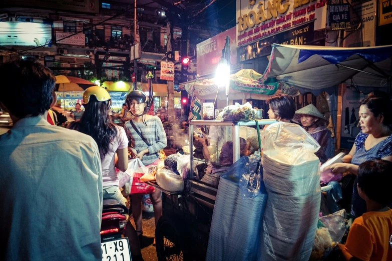 people stand near a market selling food at night