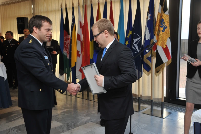 two men shake hands in front of flags