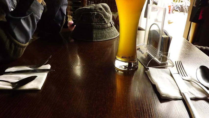 a man taking a glass of beer on top of a wooden table