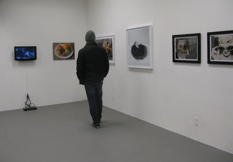 a man is walking down a room with four paintings on the wall