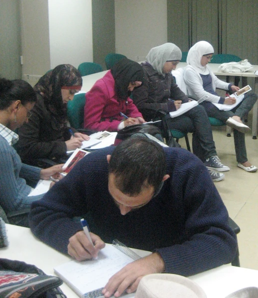 people sitting in a row, writing on notebooks
