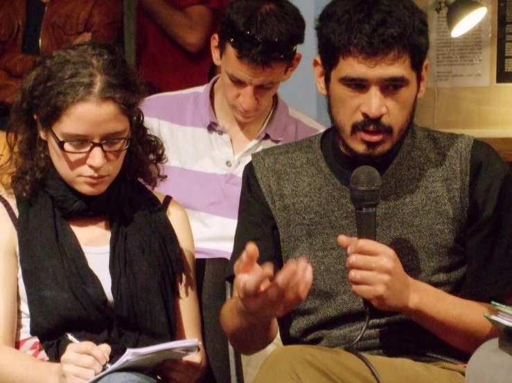 three people sitting in a row and a man talking into a microphone