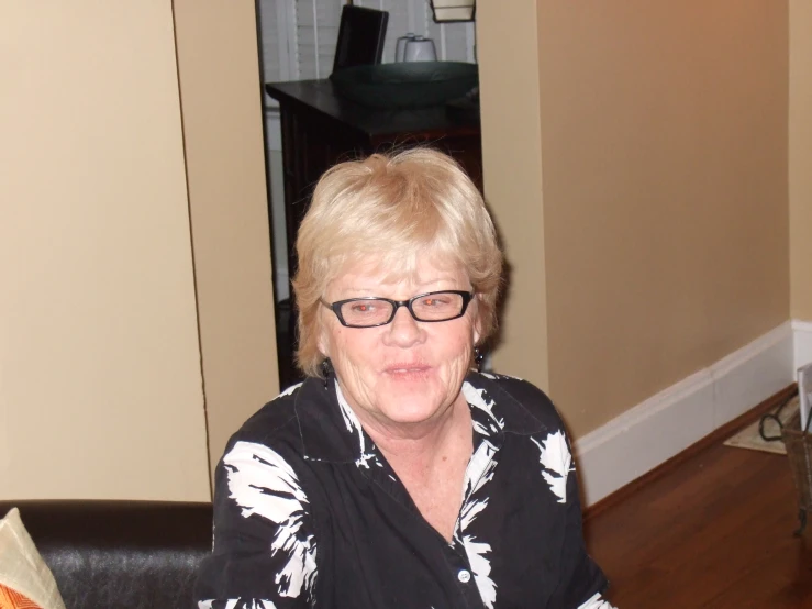 an elderly woman with glasses sits and looks off into the distance