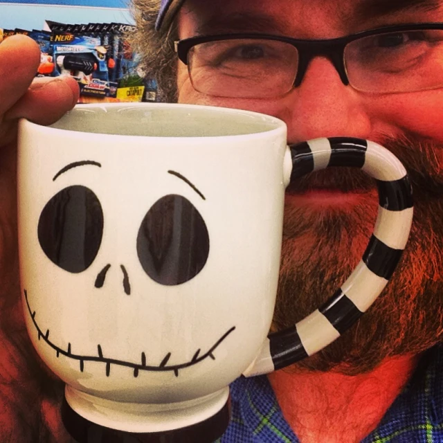a man is holding a coffee mug decorated with a skull
