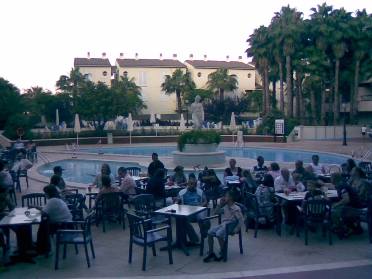 a group of people sitting at tables in front of a swimming pool