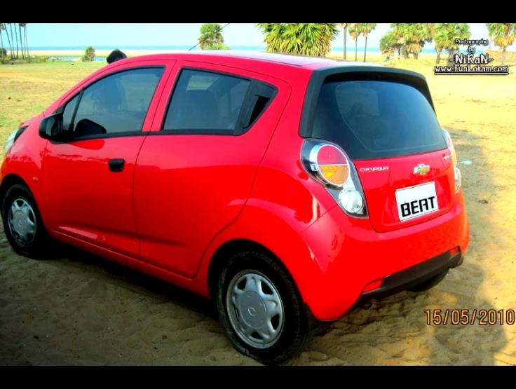 the small red car is parked in the dirt