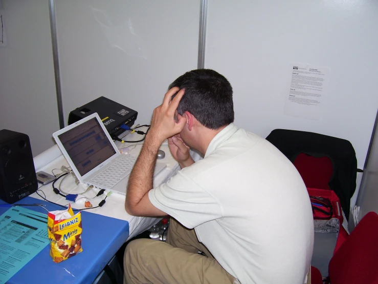 man sitting at desk holding head with hands near his eyes