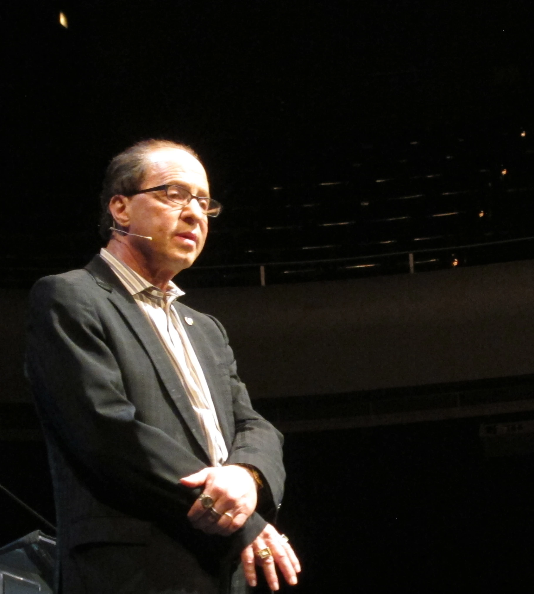 a man in glasses with a suit and tie stands at a podium