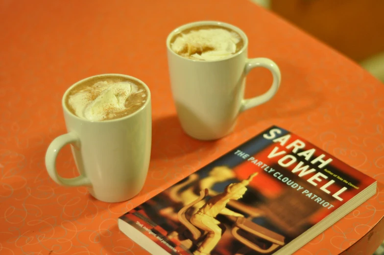 two mugs of drink sit near a book about the fiction