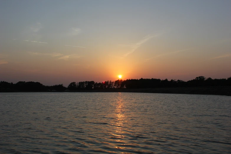 a sunrise is seen on the lake next to the forest