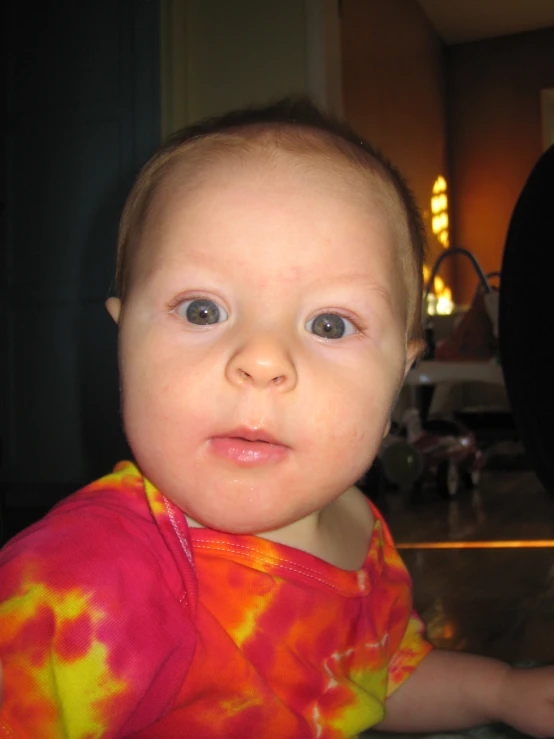 a baby with blue eyes has tie - dye t - shirt on