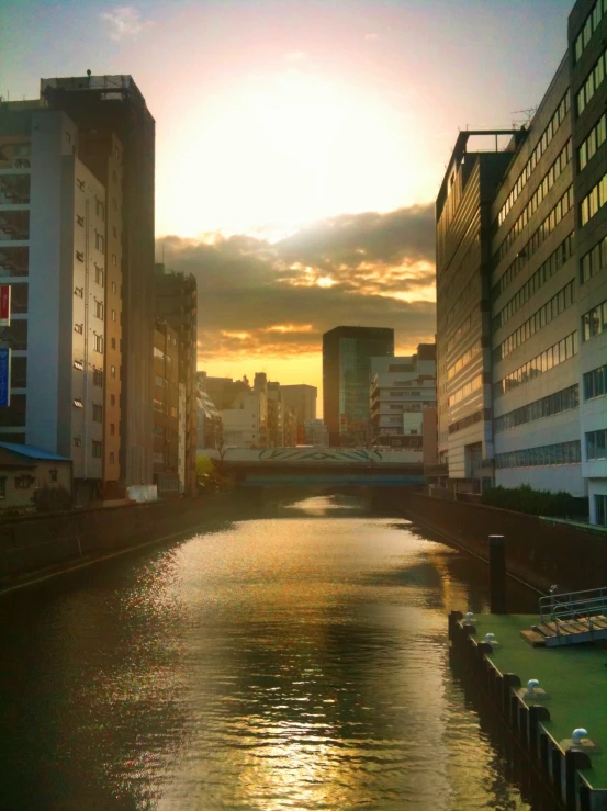 the sun is setting on the river and buildings are beside it