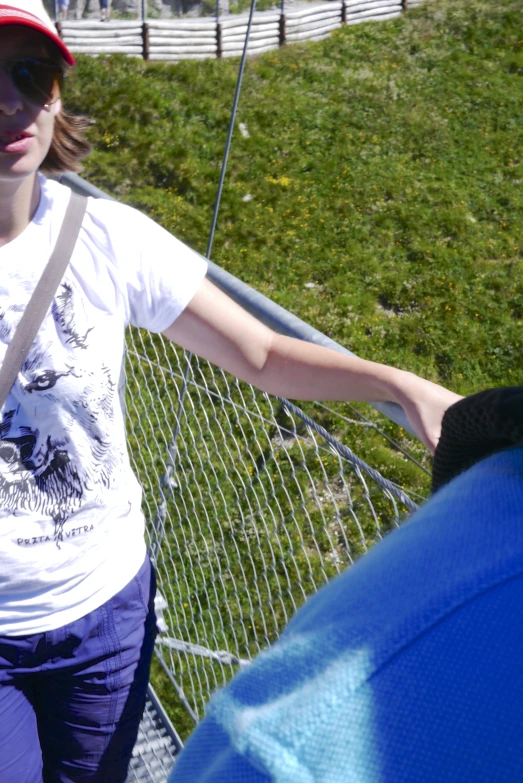 a girl leaning against the chain link fence wearing a hat