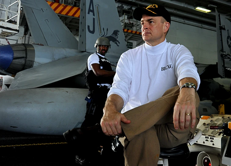 a man in black hat and cap next to airplane on deck