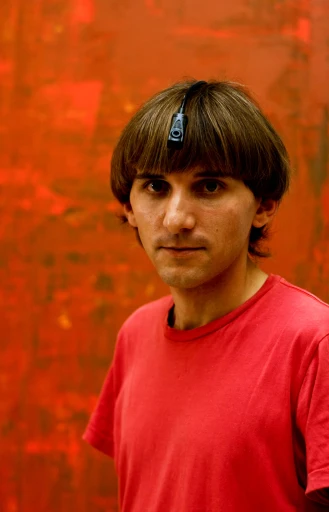 a man with black hair standing in front of a orange wall