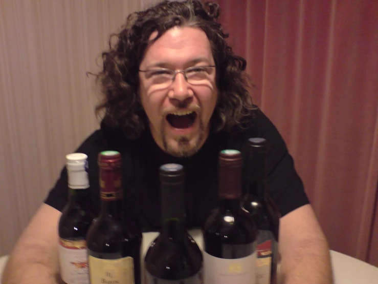 a man with glasses sitting at a table with bottles of wine