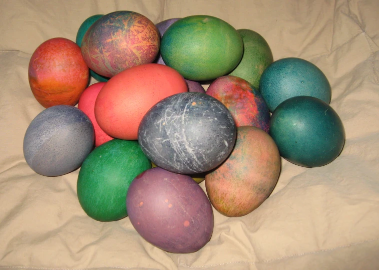 many colored eggs sitting on a cloth on a blanket