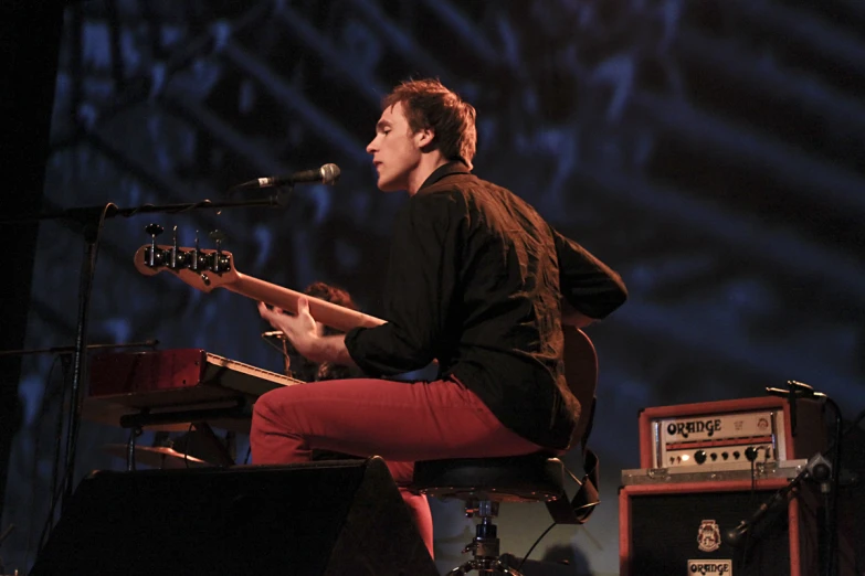 young man in brown shirt and red pants playing a guitar
