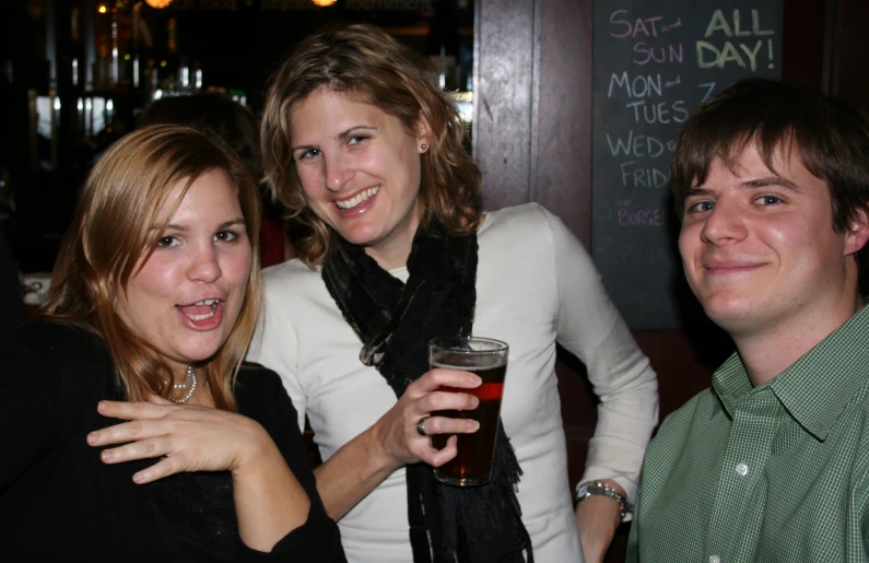 two females and one guy at a bar with a beer