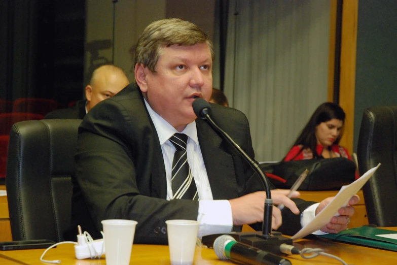 an older man is sitting at a table and talking into a microphone