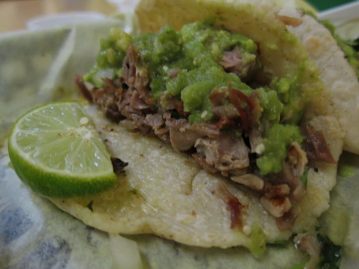 a close up of two tacos with meat, guacamole and a lime