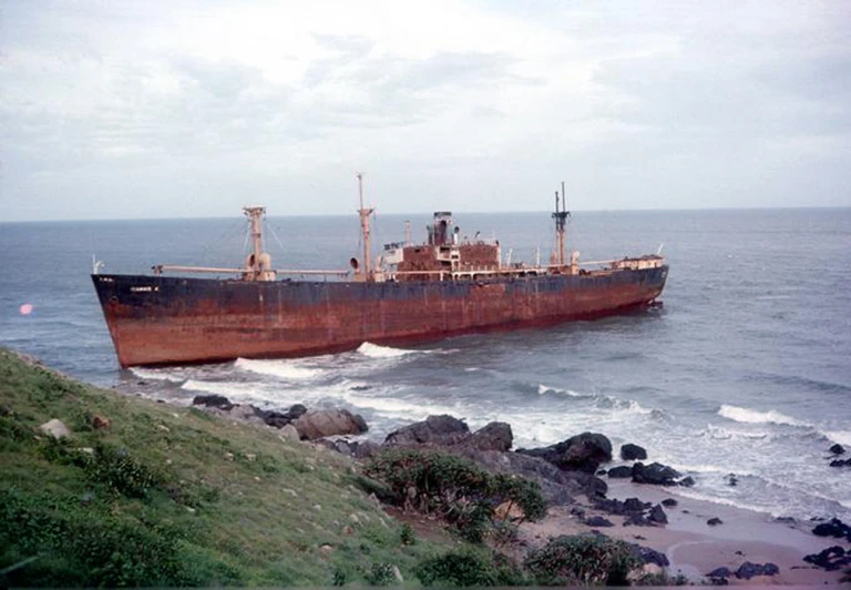 the large ship is sailing past the rocky shoreline