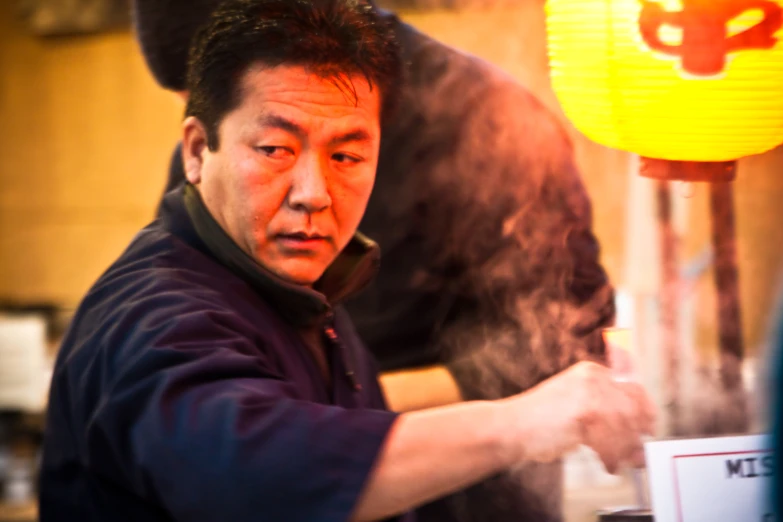 an asian man with dark hair and black shirt cooking a pot