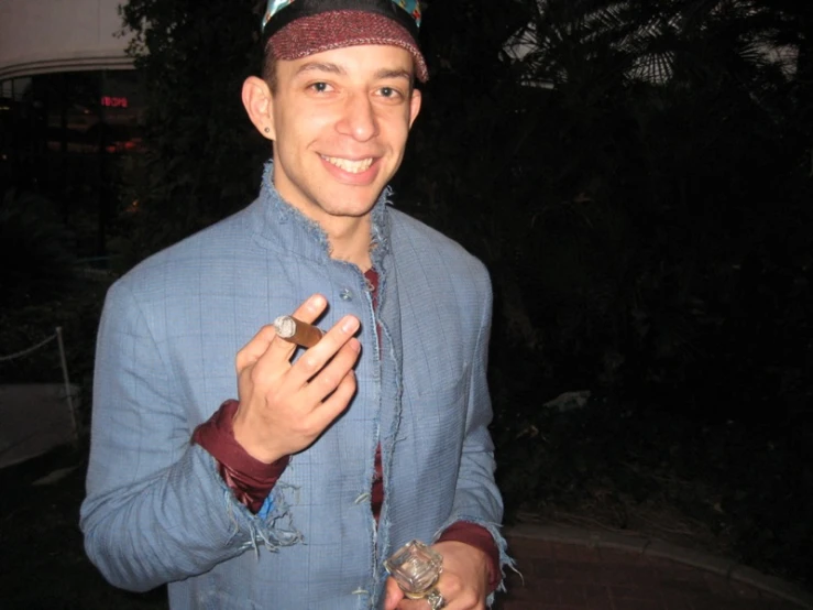 a smiling man wearing a baseball cap is holding his cigarette