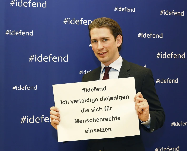 a man in a business suit holds up a sign that says defend