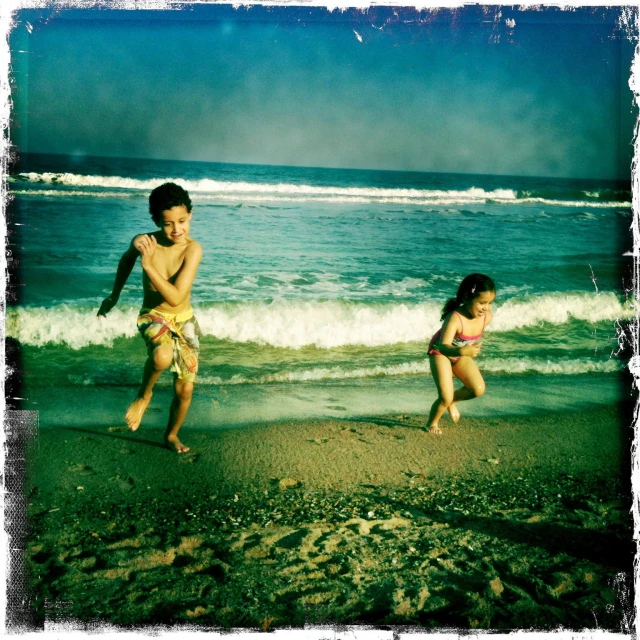 two little girls playing on the beach with the waves