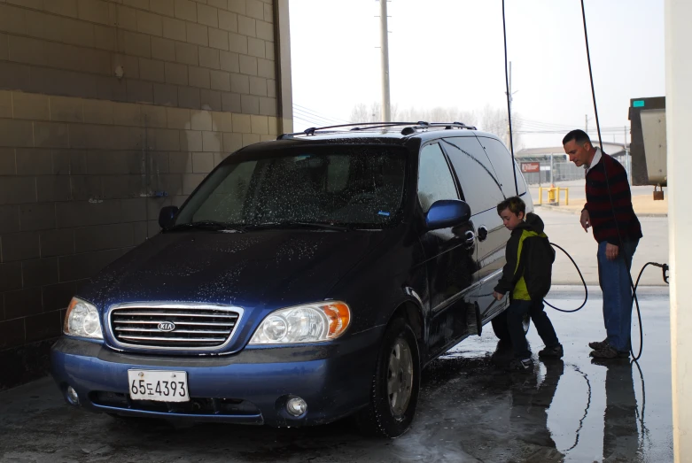 a man is washing the windshield of a blue mini van