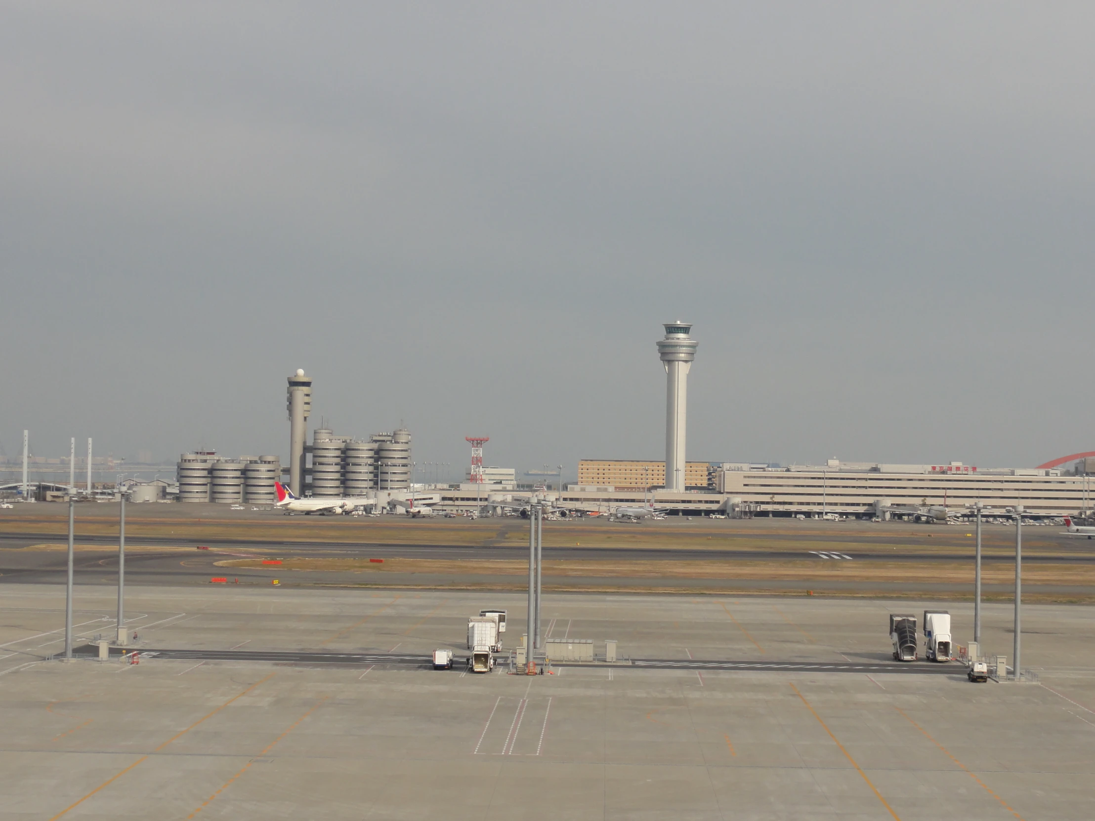 three trucks sit on the runway near the control towers