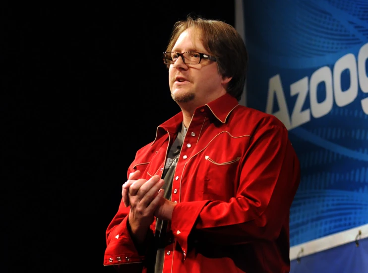 a man in a red shirt is speaking on stage