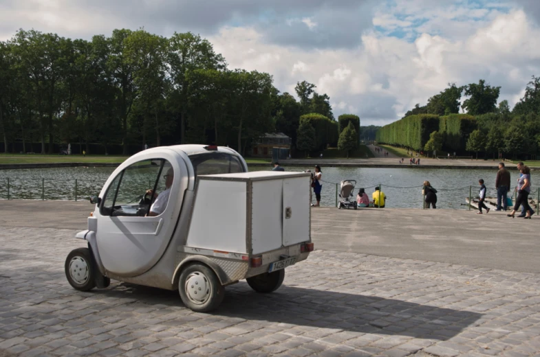 a small white car with people walking by