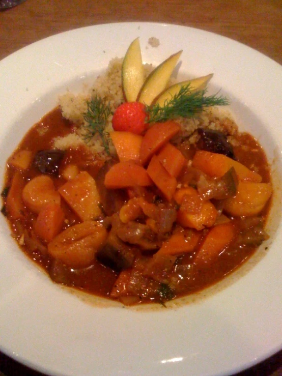 the bowl is full of soup and meat with a cherry decoration