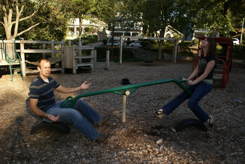 two people on playground equipment sit down in the park