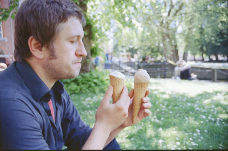 a man in blue shirt and tie eating two ice cream cones