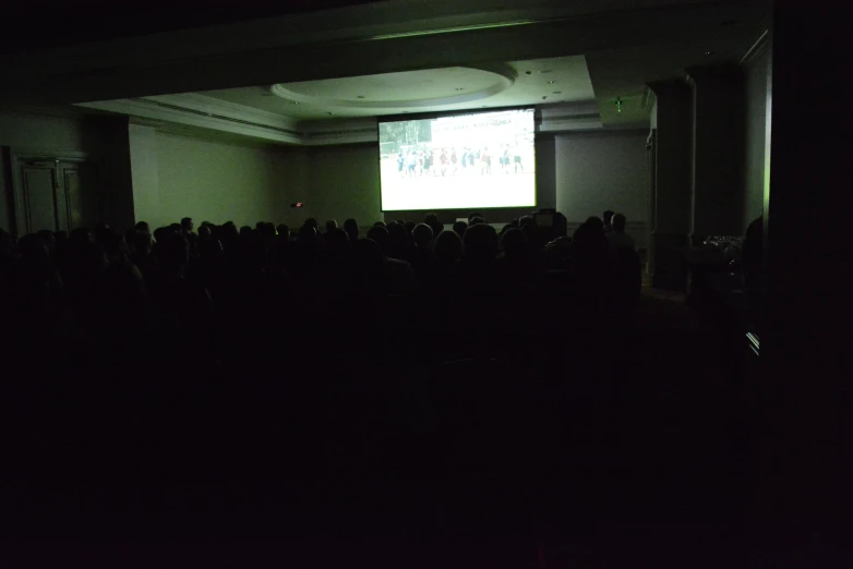 a large screen is projected in the dark room while people watch