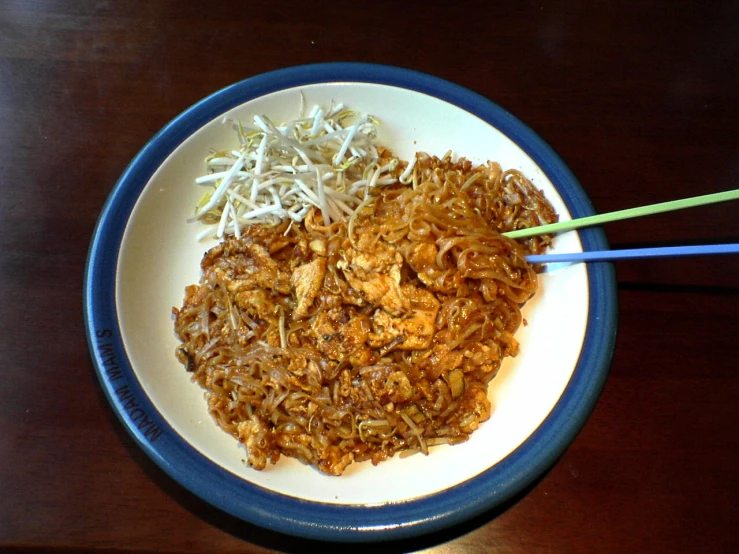 food in bowl on wooden table with chopsticks