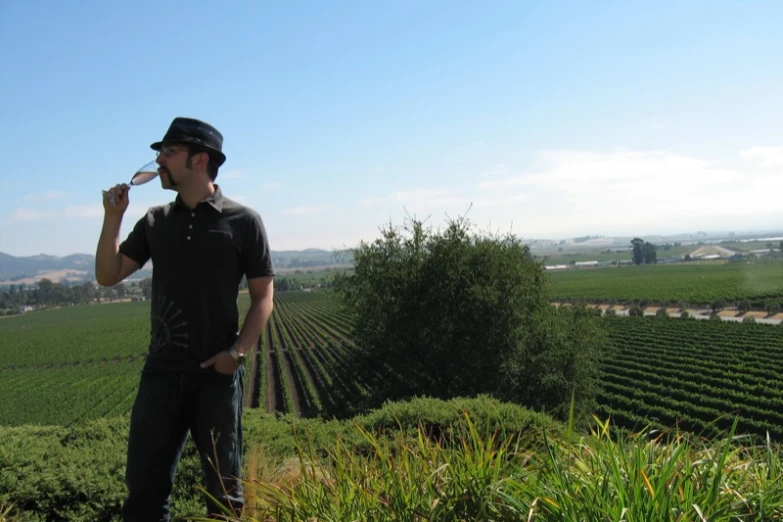 a man drinking from a bottle standing in front of a farm