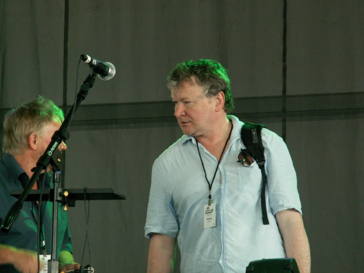 two men with headphones stand in front of microphones