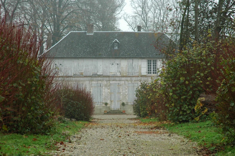 a white house in the countryside behind trees and bushes