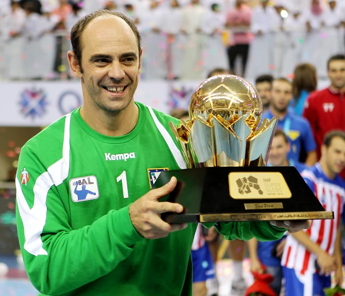 a man smiles while holding an award trophy