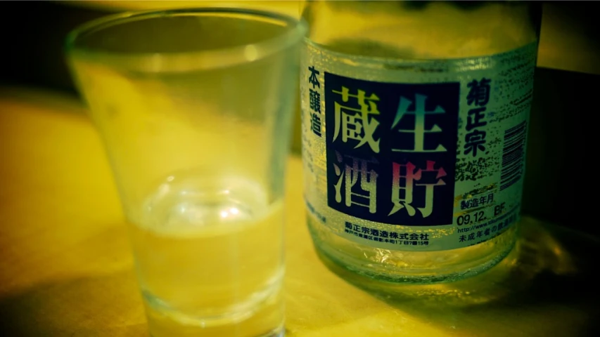a glass filled with yellow liquid and an empty bottle