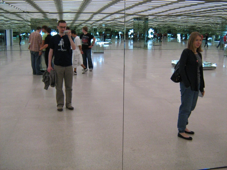 a girl and boy on cell phones standing together in the airport