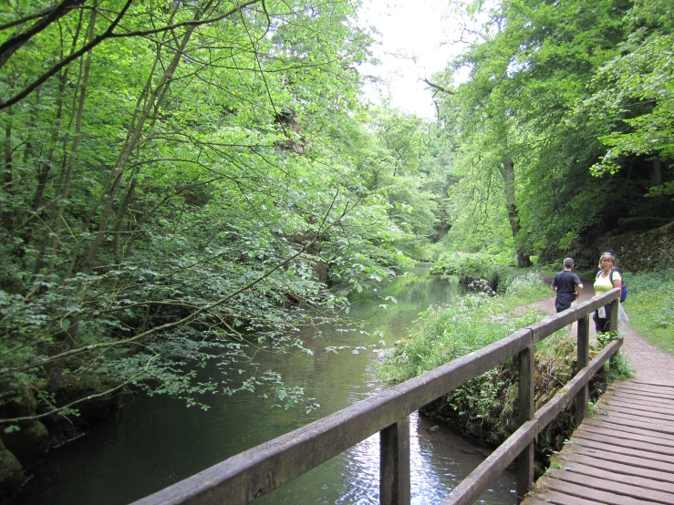 two people walk on the boardwalk above a river