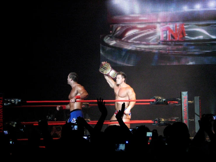 two men are holding up the same object on a big screen