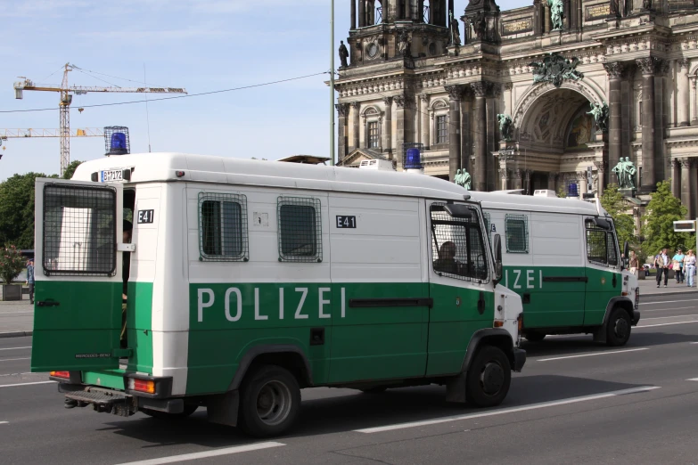 two police buses traveling on a street near a church