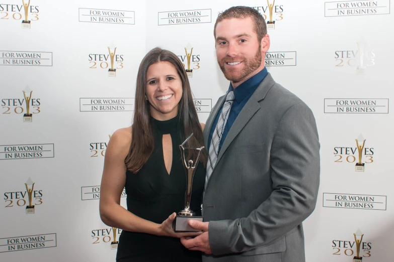 a man and woman standing on a red carpet together holding a trophy